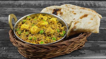 A dish of paneer curry with naan bread on a rustic wooden table.