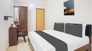 Una camera d'albergo con un letto, una scrivania con un bollitore, una sedia, un armadio e una porta.