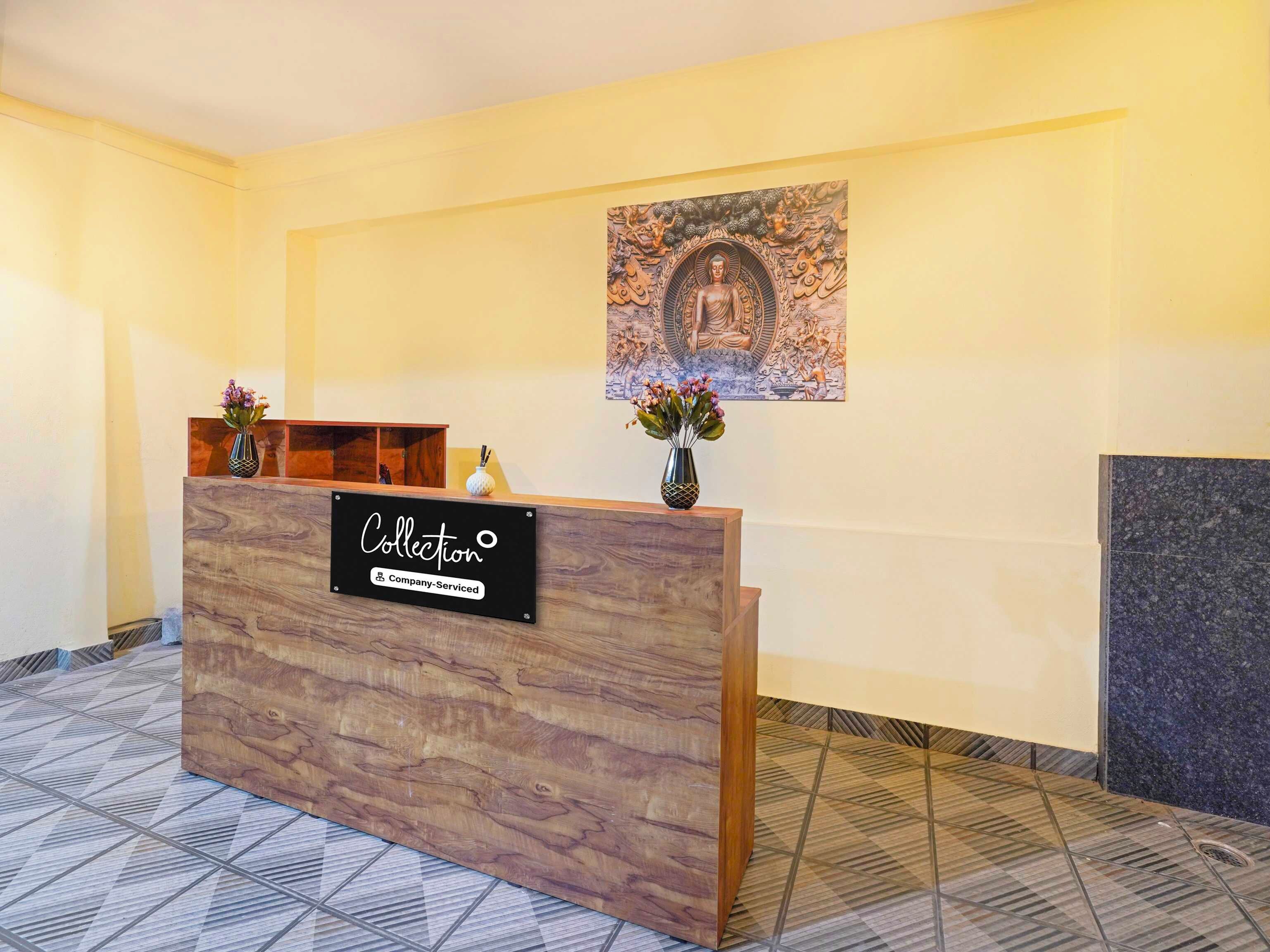 A reception desk with a 'Collection' sign, a wall-mounted artwork, and a vase with flowers.