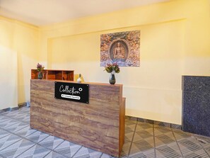 A reception desk with a 'Collection' sign, a wall-mounted artwork, and a vase with flowers. - Collection O Karmelaram Railway Station (Bengaluru)