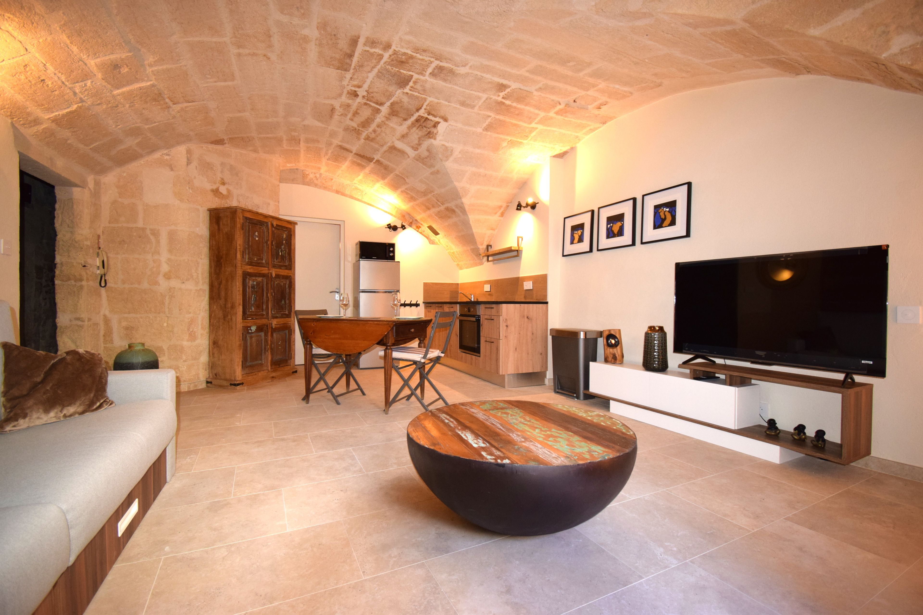 A cozy living room with a stone ceiling, a wooden dining table, a sofa, and a flat-screen TV.