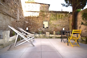 Ein Innenhof mit Steinmauern, gefliestem Boden und Gartenmöbeln, darunter ein gelber Stuhl und ein Tisch.