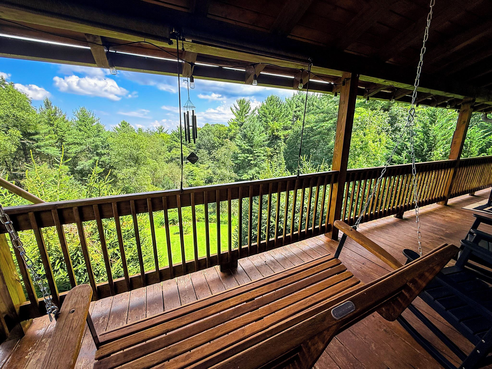 A wooden deck with a bench and a hanging light fixture, overlooking a lush green landscape.