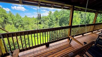 A wooden deck with a bench and a hanging light fixture, overlooking a lush green landscape.
