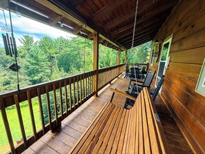 A wooden deck with a railing, outdoor seating, and a view of a forest. - Tree Top Retreat - Where Mountain Luxury Meets Adventure (Fleetwood)