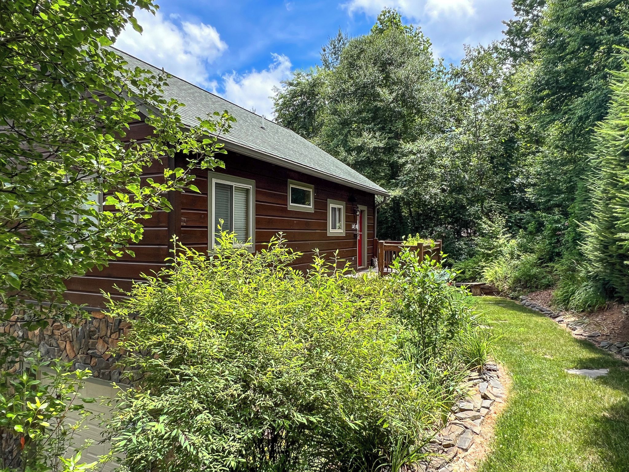 A wooden cabin with a stone foundation, surrounded by dense greenery and trees.
