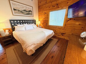 A wooden-paneled bedroom with a bed, bedside lamps, a window with blinds, and a mounted television. - Tree Top Retreat - Where Mountain Luxury Meets Adventure (Fleetwood)