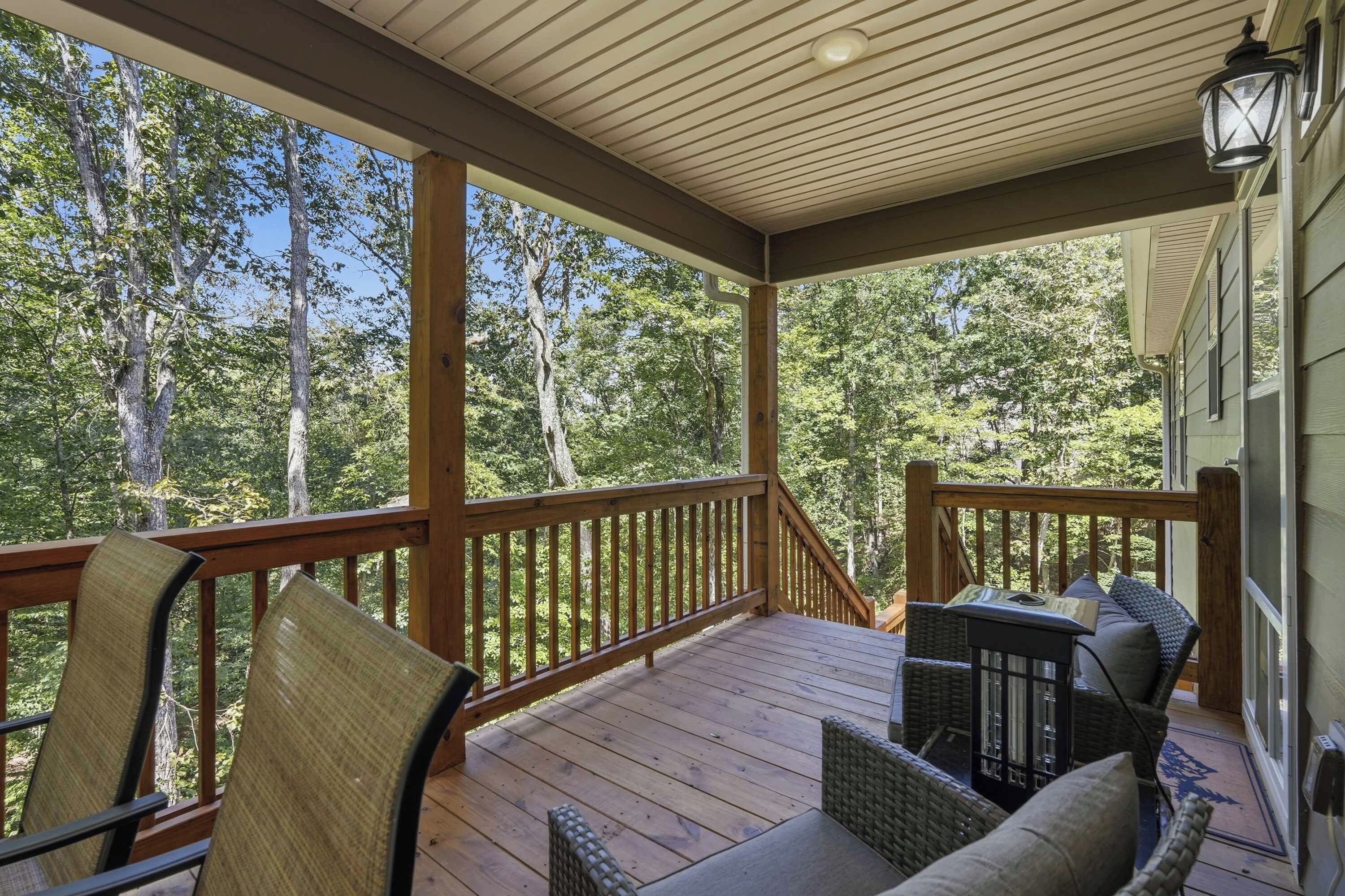 A covered porch with wooden railings, wicker furniture, and a view of a forested area.