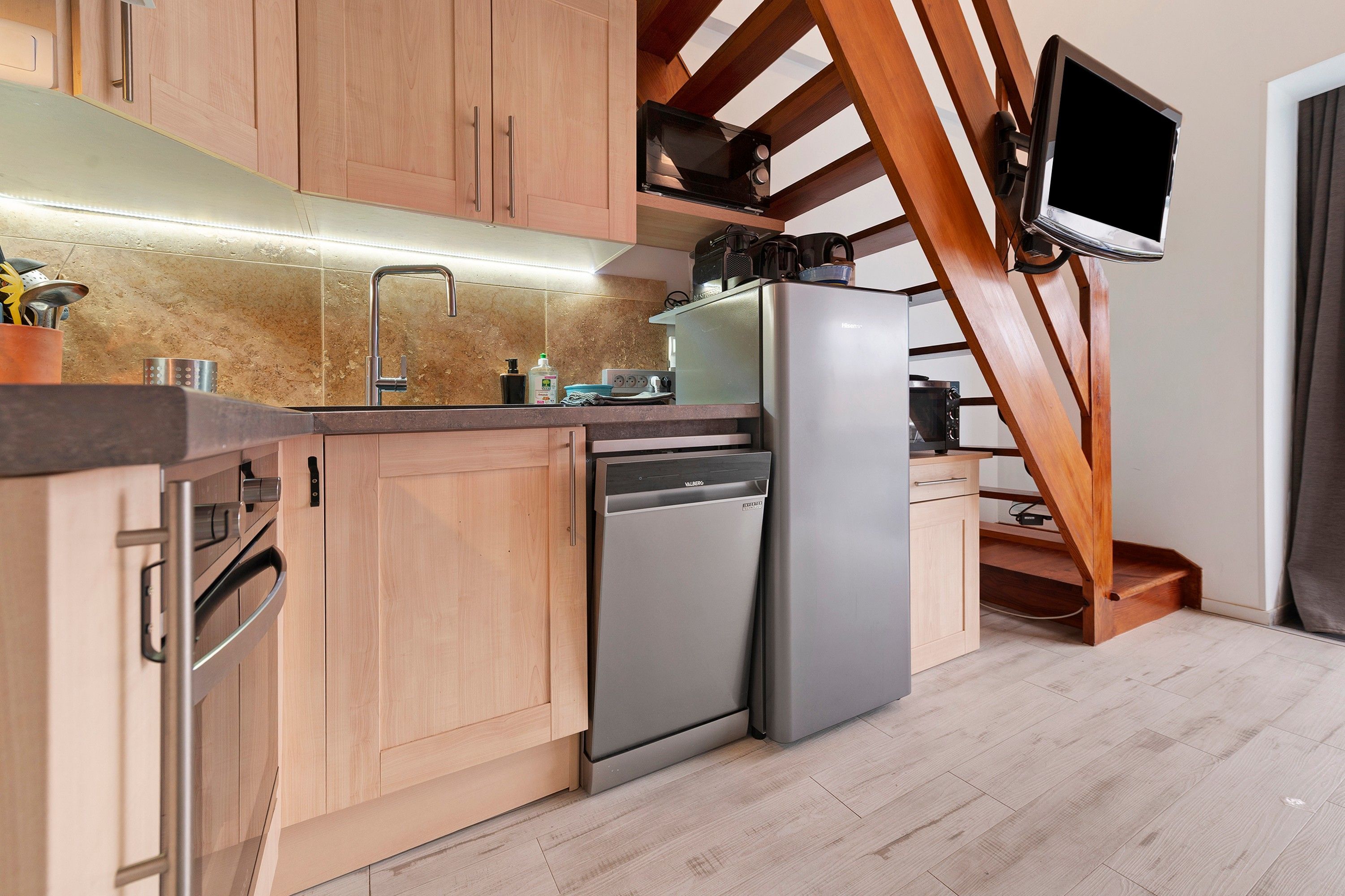 A modern kitchen with wooden cabinets, a stainless steel dishwasher, and a built-in oven.