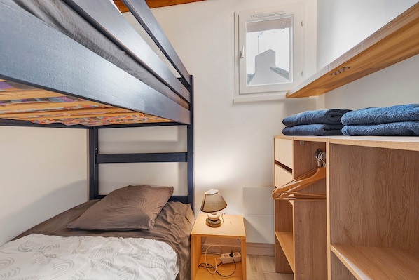 A bunk bed with a headboard, a bedside table with a lamp, and a wooden wardrobe with towels.
