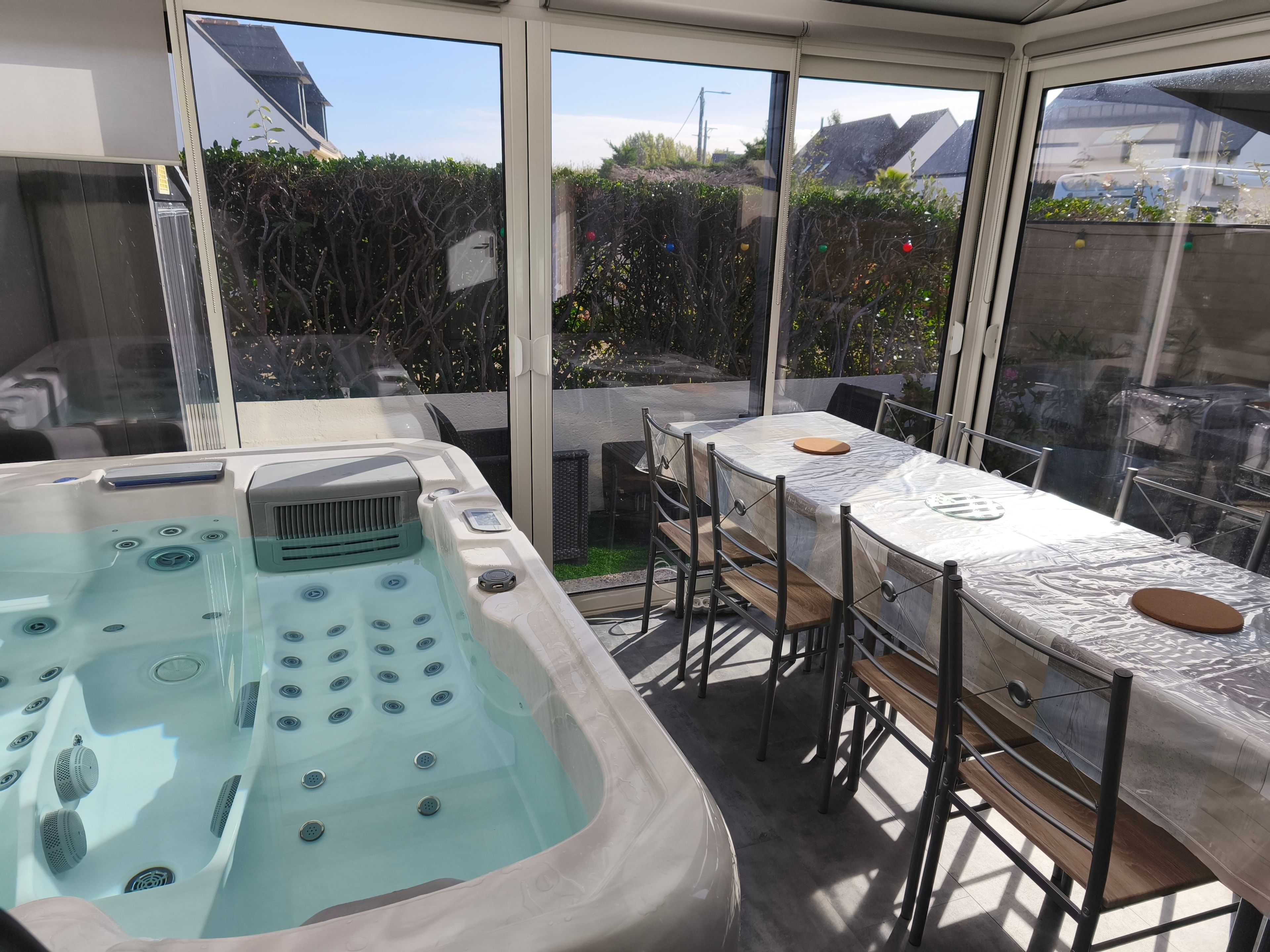 A hot tub with a table and chairs, a glass enclosure, and a view of the outside.