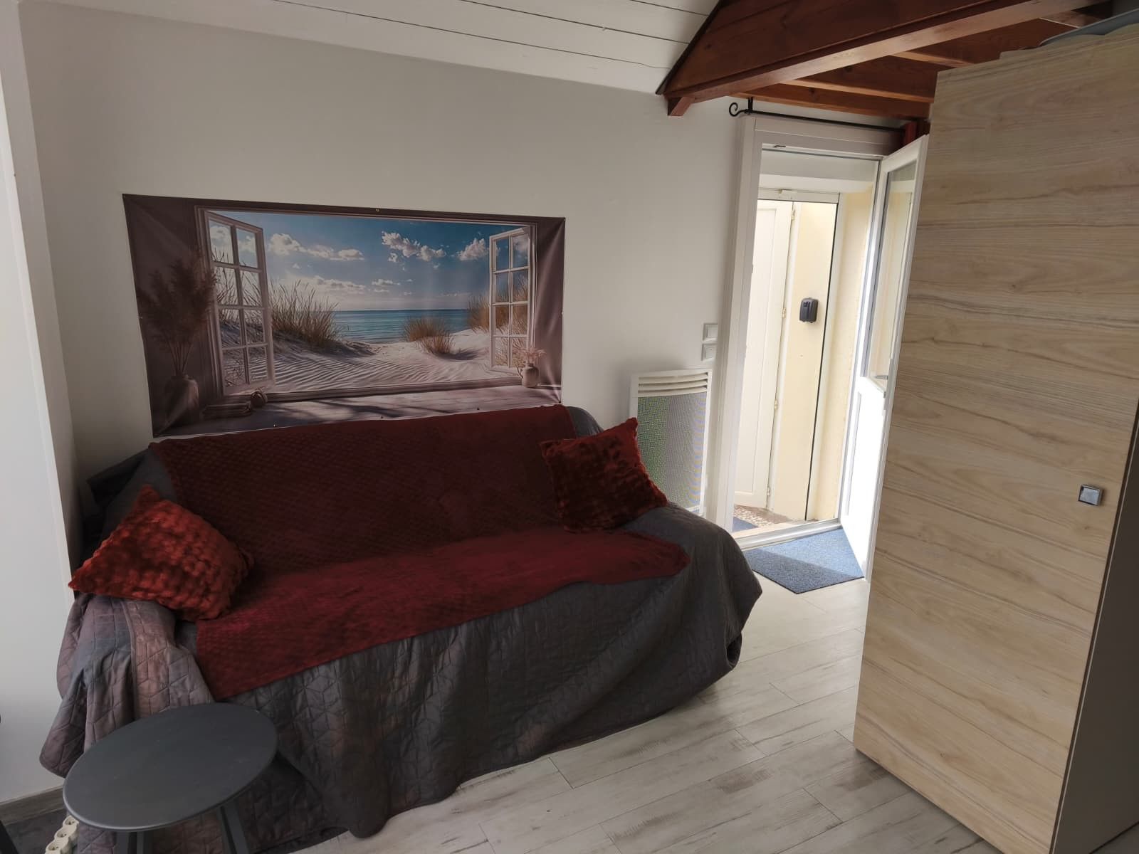 Una habitación con un ventanal grande, una puerta de madera, un sofá rojo y una mesita redonda.