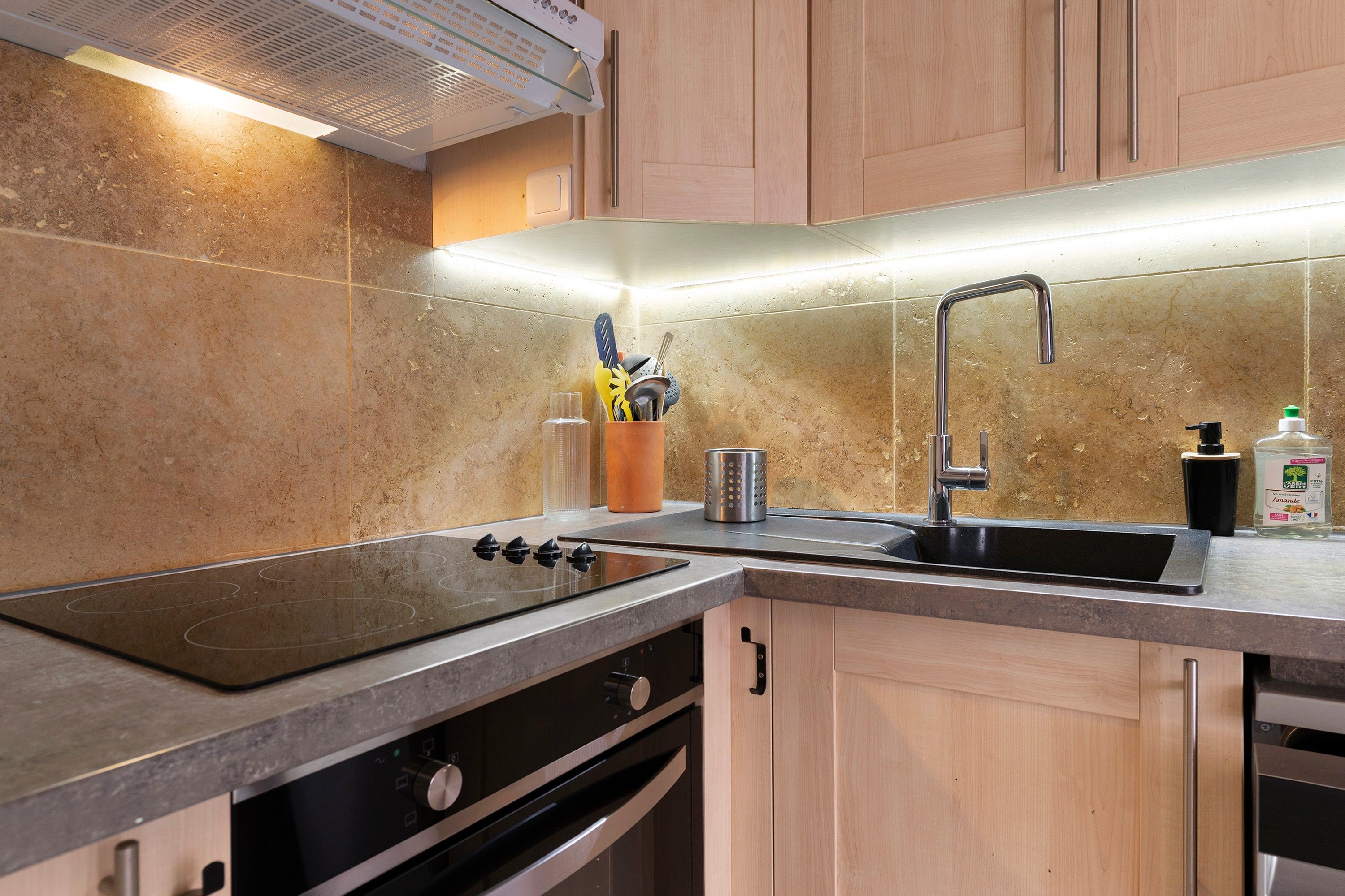 A kitchen with a stainless steel sink, a stove, and wooden cabinets.