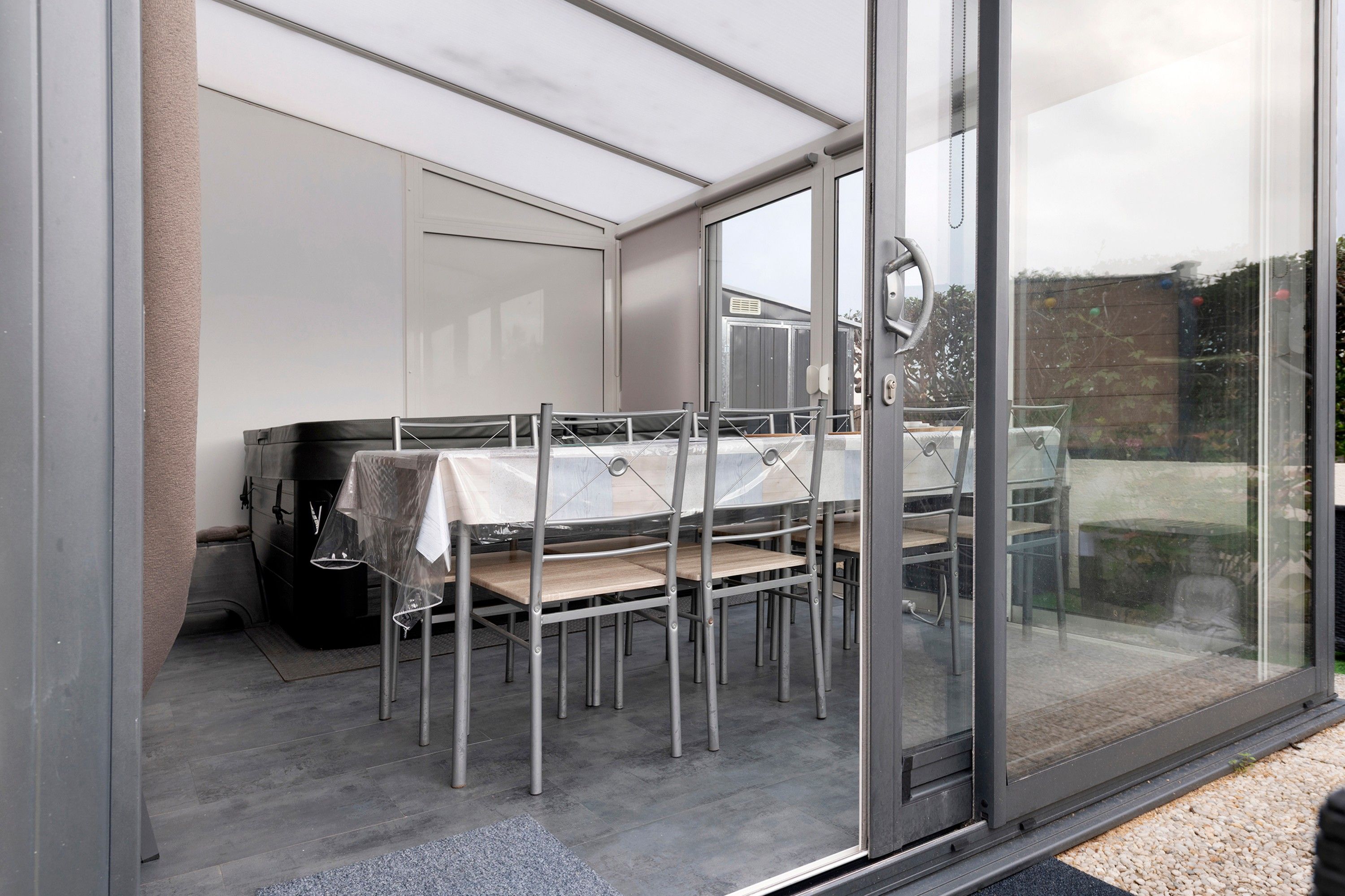 A covered outdoor dining area with a table and chairs, a grill, and a glass door leading outside.
