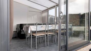 A covered outdoor dining area with a table and chairs, a grill, and a glass door leading outside.