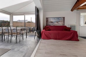 A modern living room with a red sofa, a painting of a beach scene, and a view of the outdoors.