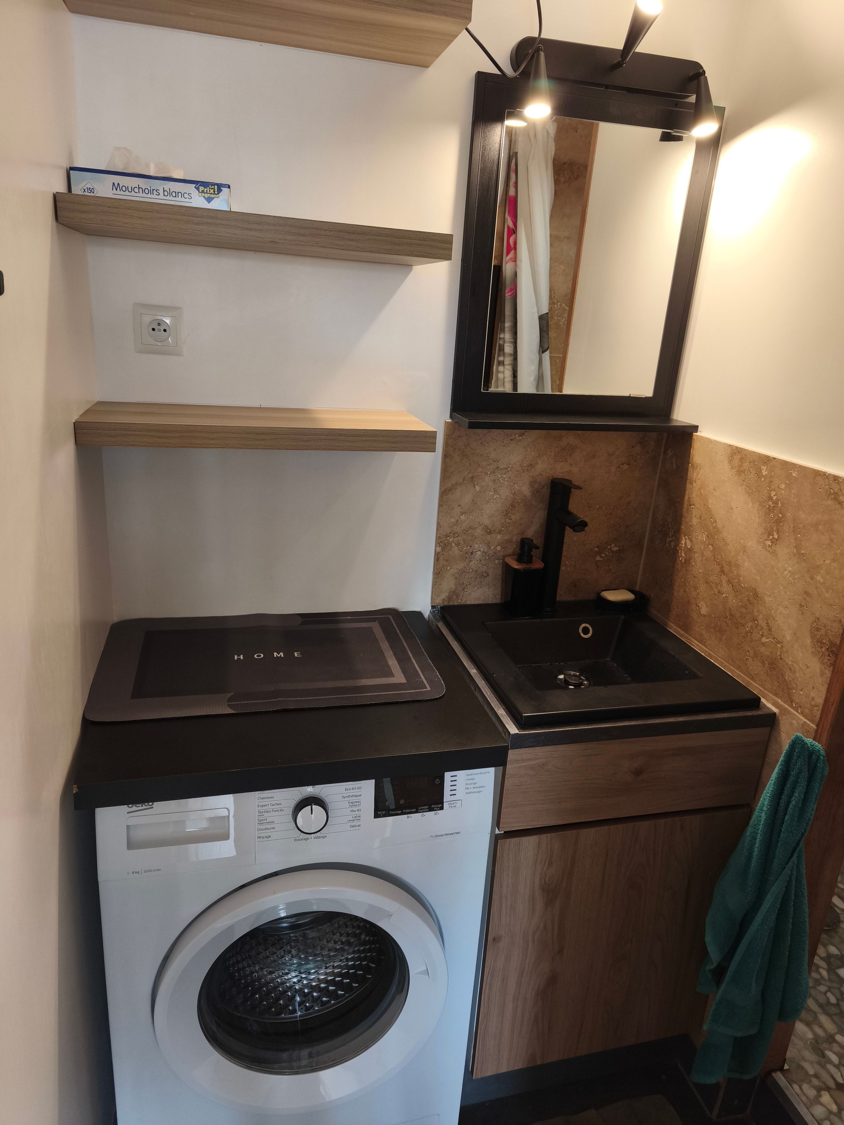Eine kleine Küchenzeile mit Waschmaschine, Spüle und Spiegel.