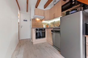 A compact kitchen with wooden cabinets, a stainless steel refrigerator, and a built-in oven.
