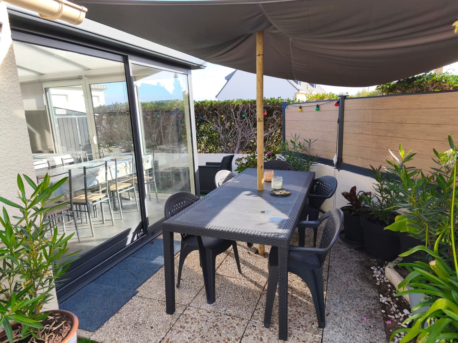 Eine Terrasss mit Tisch und Stühlen, umgeben von Blumentöpfen und einem Holzzaun.