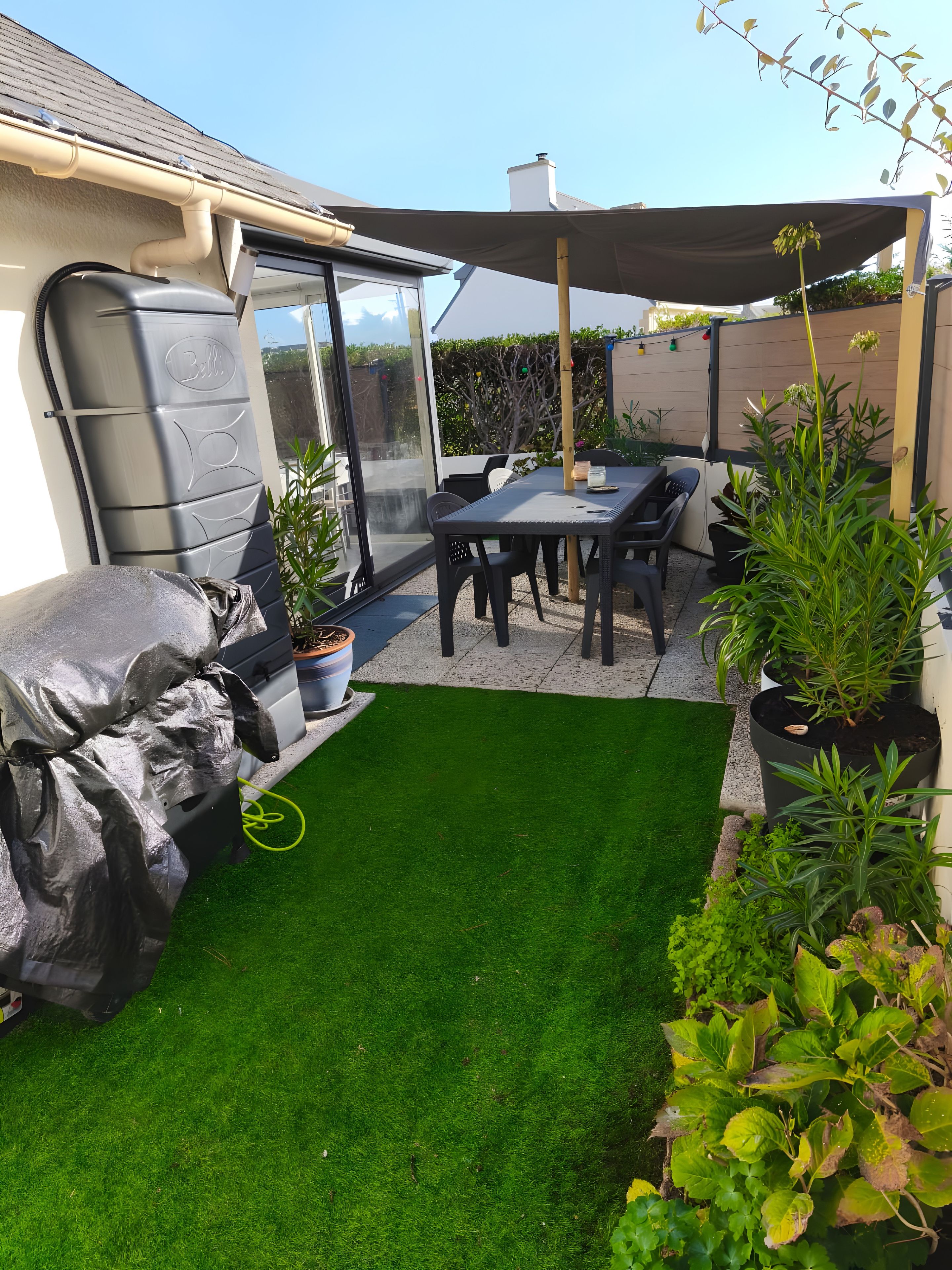 Eine Terrasse mit Tisch, Stühlen, einem Grill und Kübelpflanzen.