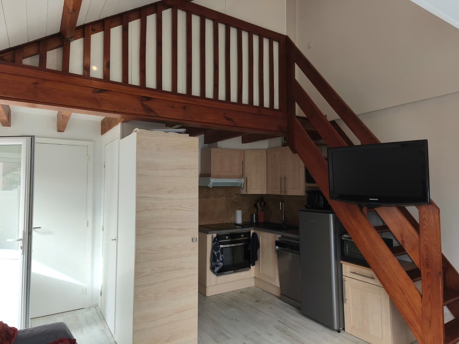 A compact kitchen with wooden cabinets, a stainless steel refrigerator, and a built-in oven.