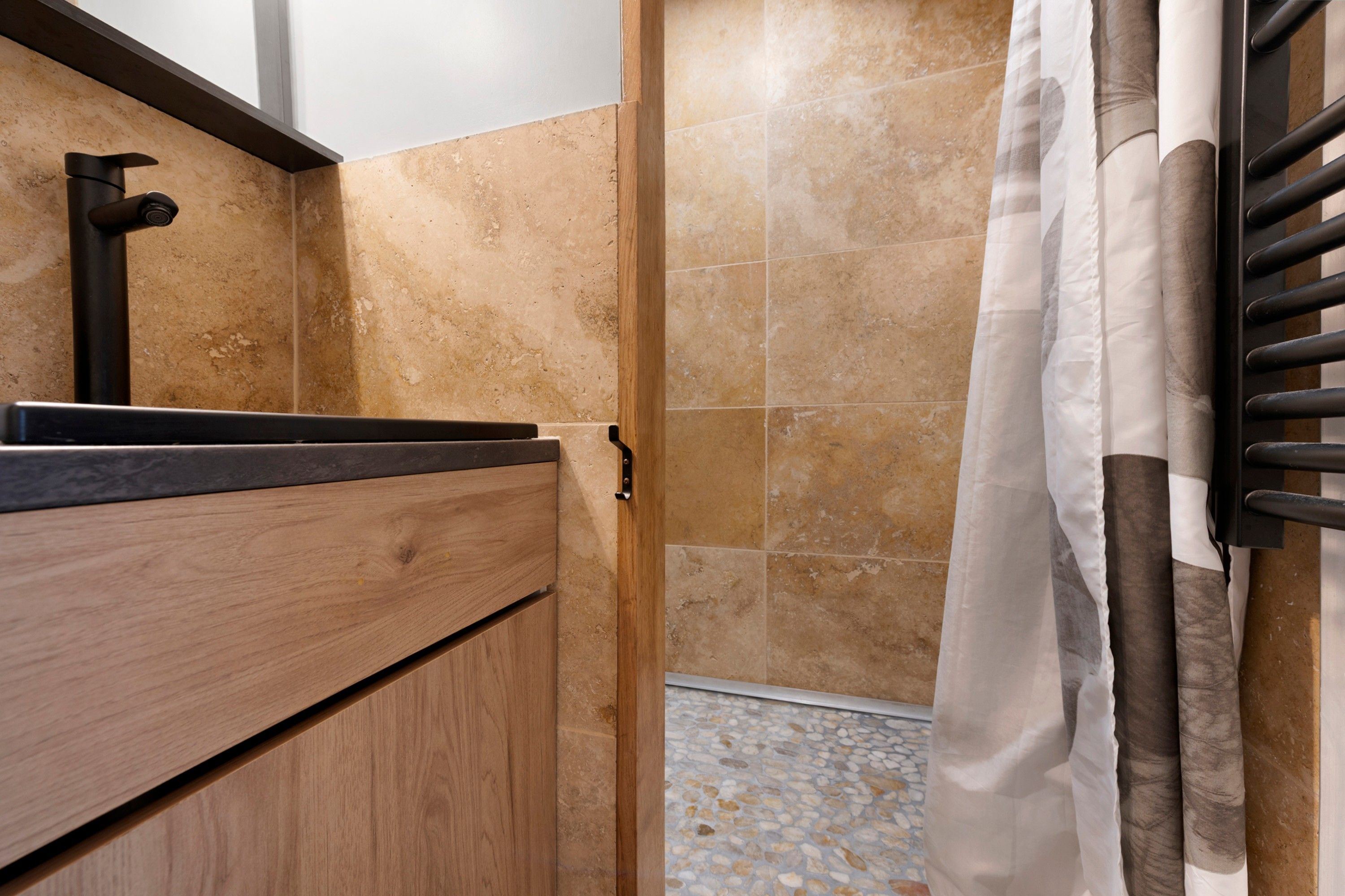 Une salle de bain avec un meuble-lavabo en bois, un robinet noir et un espace douche doté d’un sol carrelé.
