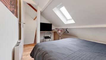 A bedroom with a sloped ceiling, a skylight, a bed, a chair, a desk, and a wall-mounted fan.