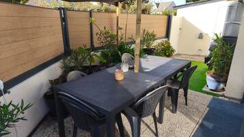 Un patio exterior con una mesa y sillas, rodeado de plantas en macetas y una valla de madera.