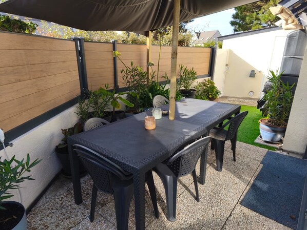 Un patio exterior con una mesa y sillas, rodeado de plantas en macetas y una valla de madera.