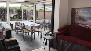 A modern interior with a dining area, a sofa, and a large window offering a view of the outdoors. - Holiday Home 'Le Cottage Des Dunes - Erdeven' with Private Terrace, Garden and Wi-Fi (Erdeven)