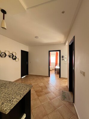A hallway with a kitchen area on the left, a door leading to another room, and a tiled floor.