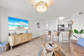 A modern living room with a flat-screen TV, wicker furniture, a round coffee table, and a kitchen area with a microwave and stove. - Key Lime Sunrise Top Floor Oceanfront 3404 (Tavernier)