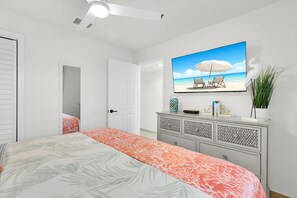 A bedroom with a bed, a TV mounted on the wall, a ceiling fan, and a door leading to another room. - Key Lime Sunrise Top Floor Oceanfront 3404 (Tavernier)