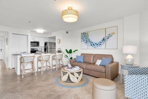A modern living room with a sofa, a round coffee table, and a dining area with chairs. - Key Lime Sunrise Top Floor Oceanfront 3404 (Tavernier)