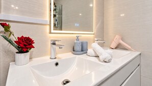 Ein modernes Badezimmer mit einem großen Spiegel, einem weißen Waschbecken und einem Föhn auf der Ablagefläche.