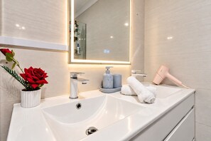 A modern bathroom with a large mirror, a white sink, and a hairdryer on the counter. - Spacious 3BR Family Home | Stylish | Free Parking (Oakhurst)