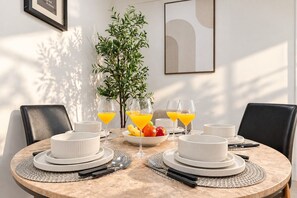 A round dining table with white plates, glasses, and cutlery, surrounded by chairs.