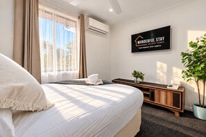 A hotel room with a bed, a bedside table, a plant, and a sign on the wall. - Spacious 3BR Family Home | Stylish | Free Parking (Oakhurst)