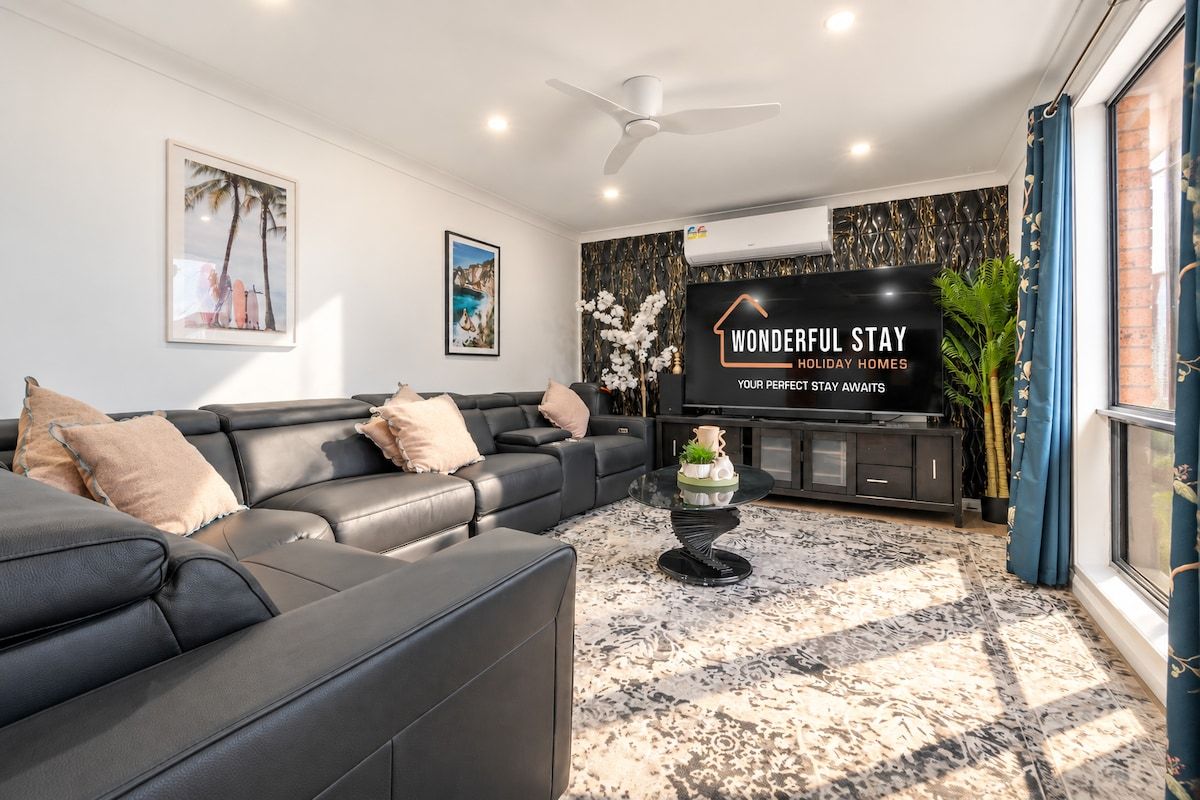 A modern living room with a black leather sofa, a glass coffee table, and a flat-screen TV displaying 'WONDERFUL STAY HOLIDAY HOMES'.