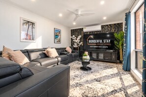 Una sala de estar moderna con un sofá de cuero negro, una mesa de centro de vidrio y un televisor de pantalla plana mostrando 'WONDERFUL STAY HOLIDAY HOMES'.