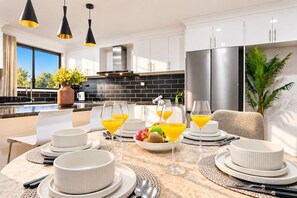 A modern kitchen with a dining area set for breakfast, featuring a large island, stainless steel appliances, and a view of the outdoors. - Spacious 3BR Family Home | Stylish | Free Parking (Oakhurst)