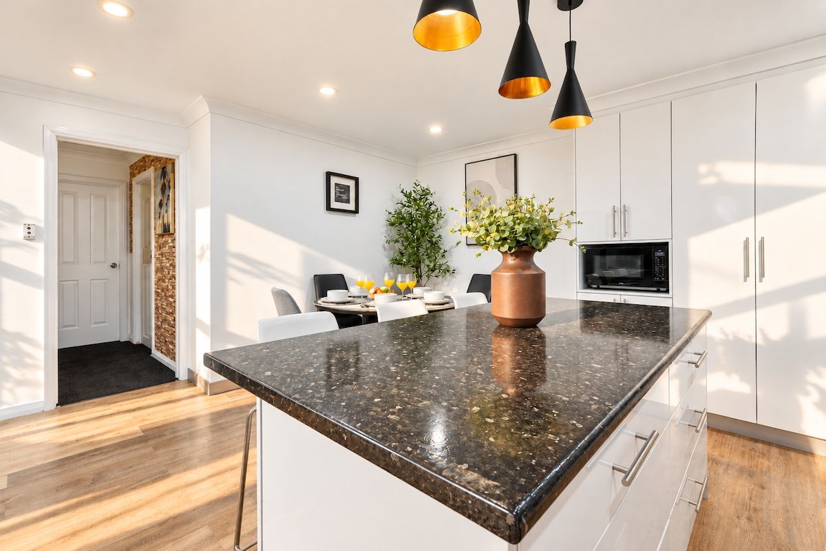 Une cuisine moderne dotée d’un plan de travail en granit, de meubles blancs et de luminaires suspendus.
