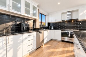 A modern kitchen with white cabinetry, black backsplash, stainless steel appliances, and a window providing natural light.