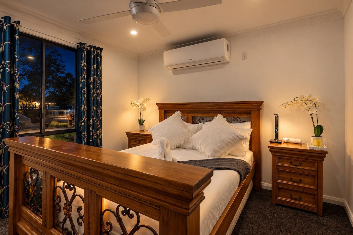 A bedroom with a bed, nightstands, a wooden bench, and an air conditioning unit.