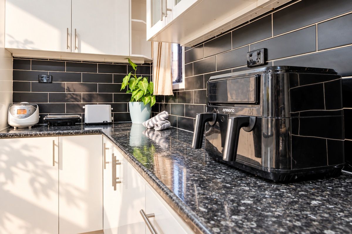 A kitchen with a black tiled backsplash, a stainless steel oven, and a countertop with a coffee maker and a plant.