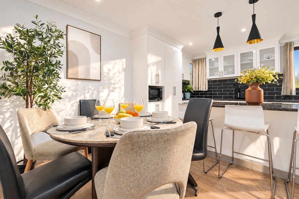 A modern kitchen with white cabinets, a black backsplash, and a dining area with a round table and chairs.