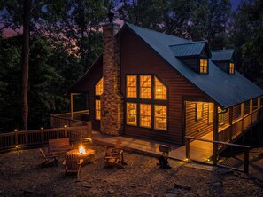 Eine Blockhütte mit einem Steinkamin, großen Fenstern und einer Terrasse mit Sitzgelegenheiten.