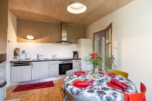 A compact kitchen with modern appliances, a dining area with a table set for two, and a wooden ceiling. - Lou Flaujer Cottage: Mountain View, Private Terrace & Wi-Fi in Pont-les-Bains (Salles-la-Source)