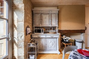 A compact kitchen with white cabinetry, a microwave, and a small dining area with a chair and table. - Lou Flaujer Cottage: Mountain View, Private Terrace & Wi-Fi in Pont-les-Bains (Salles-la-Source)