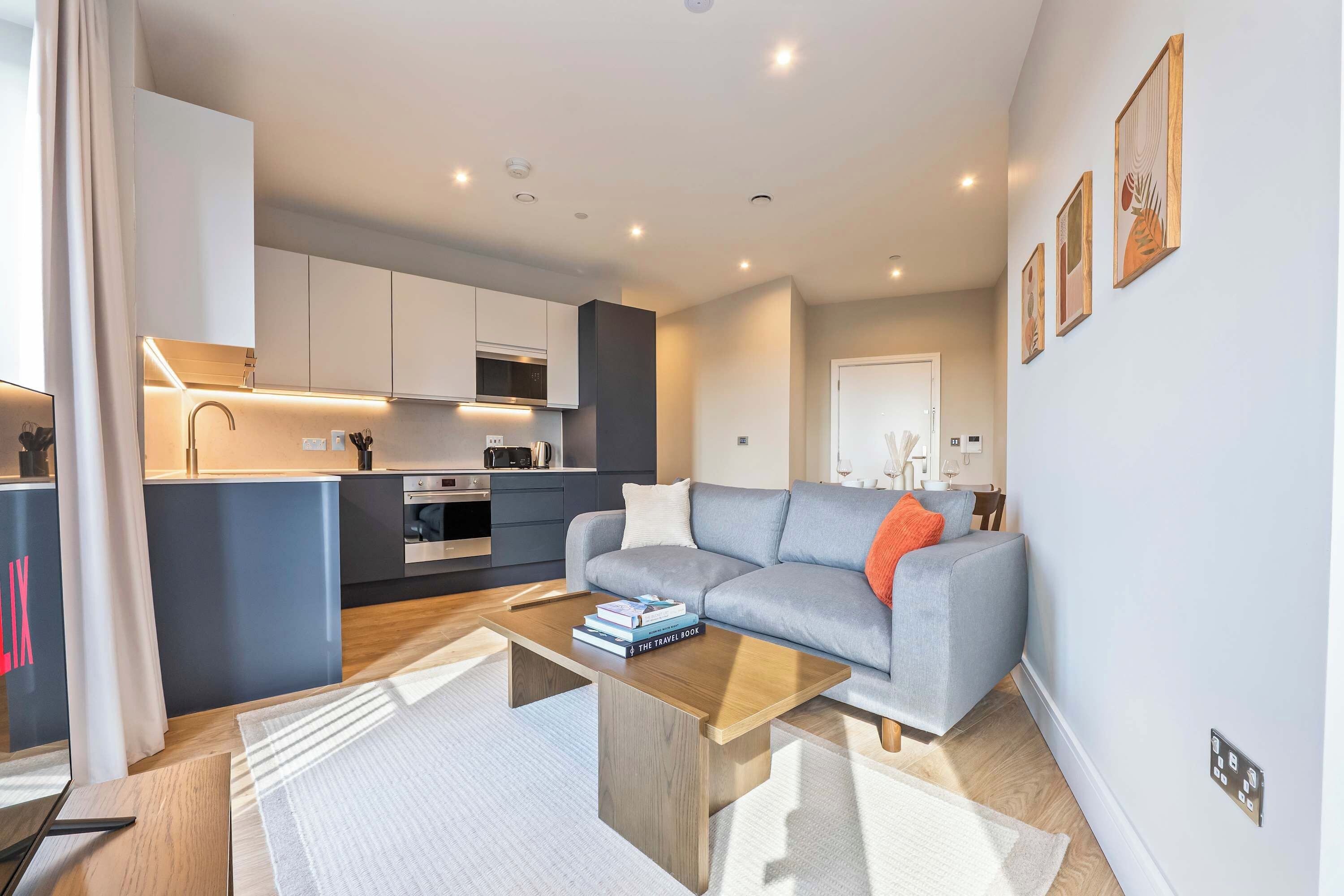 A modern living room with a grey sofa, a coffee table, and a kitchen in the background.